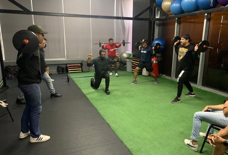 Miguel demostrando de rodillas la técnica de un ejercicio frente a alumnos con barra